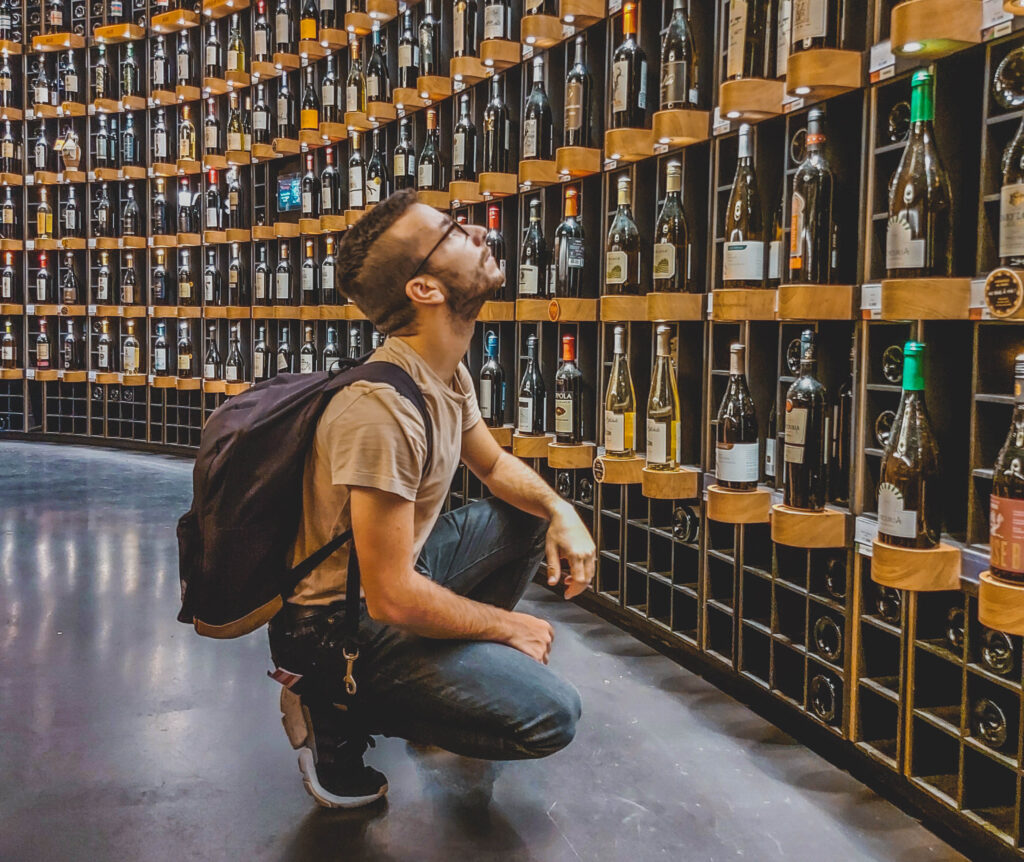 liquor-store-man-looking-up-at-wall-of-bottles-cropped
